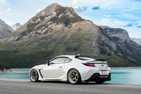 White sports car on a road with mountains and lake in the background